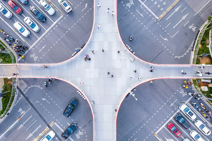 Aerial view of a large pedestrian overpass crossing above a busy intersection with cars and people visible on roads and walkways.